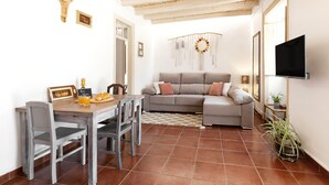 Un salon avec un canapé, une table à manger et des chaises, un téléviseur fixé au mur et une plante en pot.