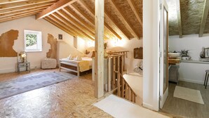 Une pièce avec des poutres apparentes, un lit, un bureau et une fenêtre donnant sur les arbres.
