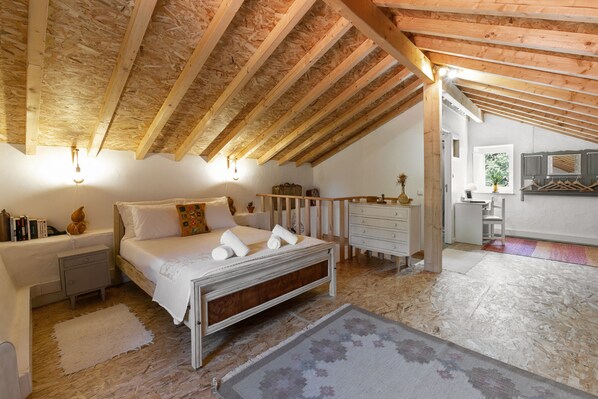 A bedroom with a wooden ceiling, a bed with white linens, a bedside table, and a nightstand.