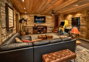 A cozy cabin interior with a leather sofa, a television, and a game room area.