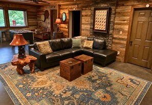 A cozy living room with a leather sectional sofa, a coffee table, a patterned rug, and a foosball table in the background.