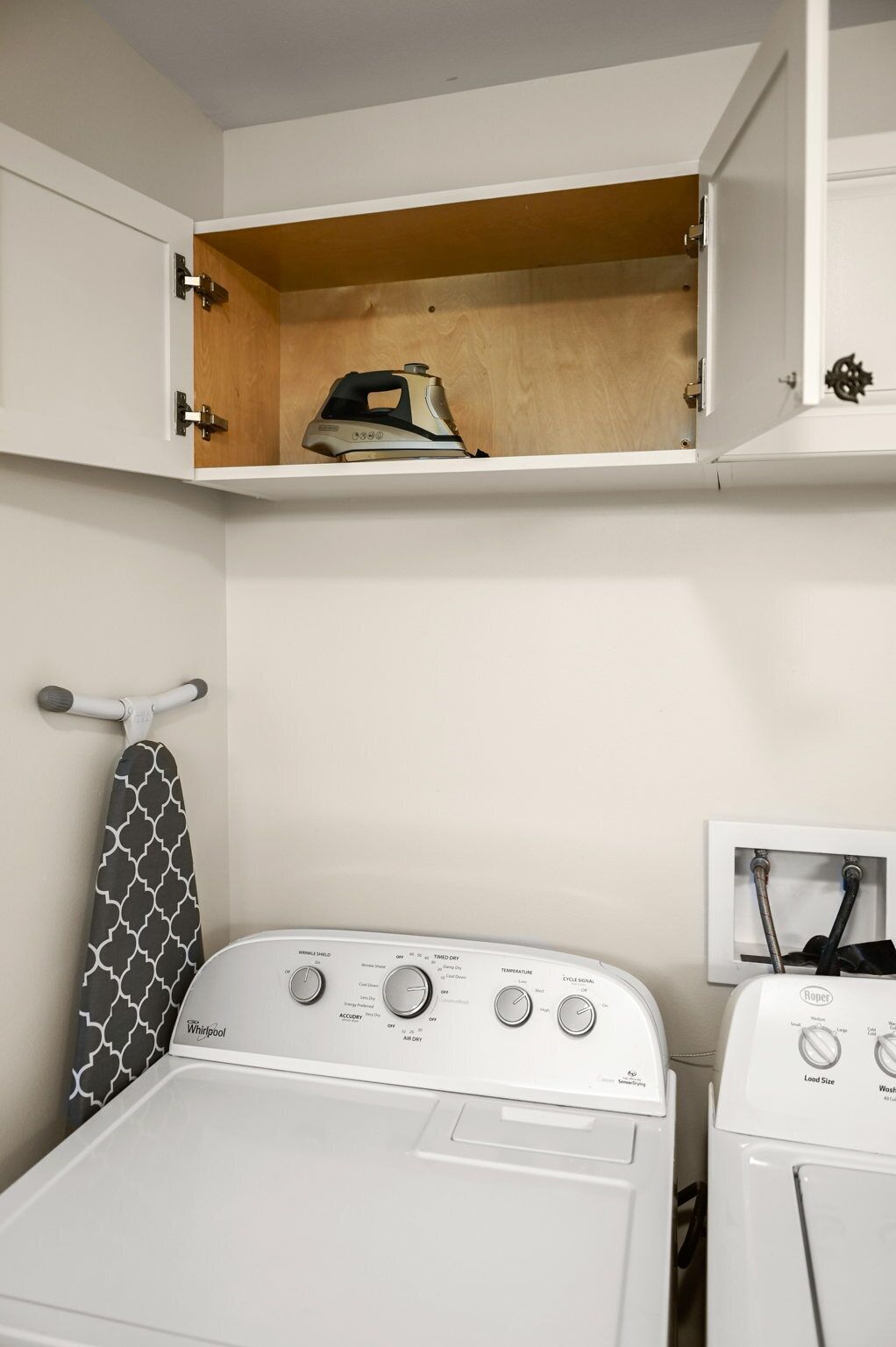 Un espace buanderie équipé d’un lave-linge et d’un sèche-linge Whirlpool, d’une étagère en bois au-dessus du lave-linge et d’un porte-serviettes avec une serviette à motifs.