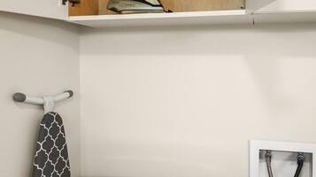 Un espace buanderie équipé d’un lave-linge et d’un sèche-linge Whirlpool, d’une étagère en bois au-dessus du lave-linge et d’un porte-serviettes avec une serviette à motifs.