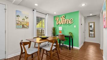A dining area with a wooden table and chairs, a green accent wall with the word "Wine," and a painting of a tropical scene.