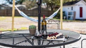 Une table ronde en métal, avec une bouteille de vin, des verres, une petite plante en pot et un morceau de fromage accompagné de raisins.