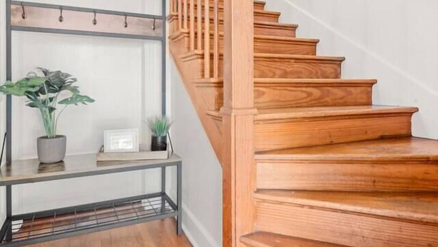 Un escalier en bois avec une rampe en métal et une étagère ornée de plantes et d’un cadre photo.
