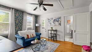 Un salon avec un canapé bleu, un ventilateur de plafond, un tapis à motifs et un plancher en bois.