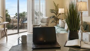 Ein modernes Wohnzimmer mit einem Laptop auf einem Glastisch, einer Kaffeetasse, einer Topfpflanze und einem Sofa mit Kissen.
