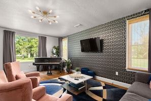 A living room with a piano, sofas, a TV, and a patterned wall.
