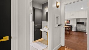 A hallway leading to a kitchen with white cabinets, a microwave, and a dining area with a table and chairs. - 1 Acre Estate Across the Lake from LSU (Baton Rouge)