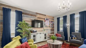 Un salon moderne avec un téléviseur à écran plat, un mur d’accent en bois, un lustre et des rideaux bleus.