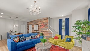 Un salon moderne avec un canapé bleu, des fauteuils jaunes, une table basse ronde et un tapis rouge.