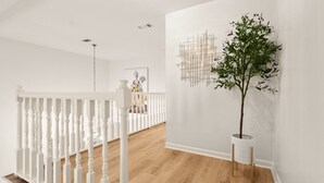 Interior moderno com piso de madeira, corrimão branco e uma planta em vaso.