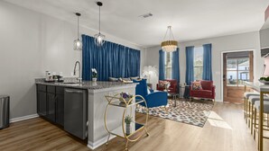 Una cocina moderna con una isla central, un comedor con una silla roja, y una sala de estar con un sofá azul.