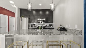 Una cocina moderna con encimeras de granito, electrodomésticos de acero inoxidable y taburetes de barra de vidrio transparente.