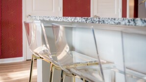 Una cocina moderna con encimera de mármol, taburetes altos de cristal y un letrero de neón.