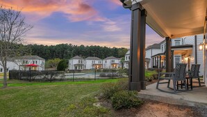 Un barrio residencial con casas, un patio cercado y un porche cubierto con mobiliario exterior.