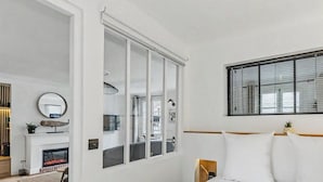 A modern hotel room with a large sliding glass door, a bed with white linens, a small bedside table, and a window with blinds. - La petite source: modern apartment in the heart of Honfleur (Honfleur)