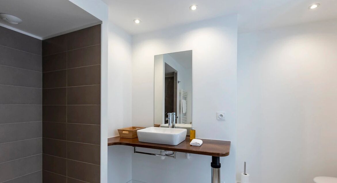 Een moderne badkamer met een witte wastafel, een spiegel en een houten aanrechtblad.