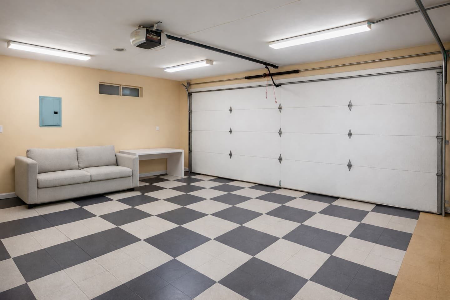 A garage with a checkered floor, a sofa, a small table, and a garage door.
