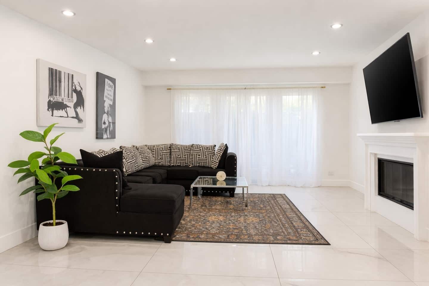 Una sala de estar moderna con un sofá negro, una mesa de centro de cristal, una planta en maceta y una chimenea.