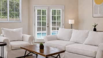 A living room with a white sofa set, a wooden coffee table, and a door with glass panels.