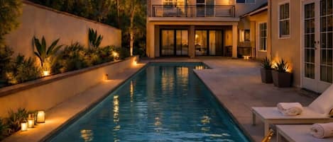 A swimming pool with a sunset view, a lounge area with chairs, and a table with drinks and candles.