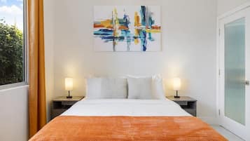 Una camera d'hotel con un letto, due comodini con lampade, una finestra con tende e un quadro appeso al muro.