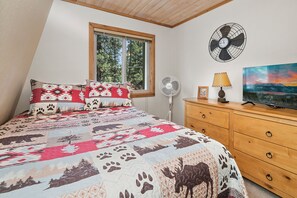 Un dormitorio con una cama, un aparador de madera, un ventilador, una lámpara y un cuadro.