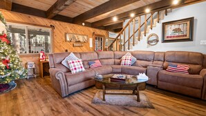 A cozy living room with a large sectional sofa, a glass coffee table, and a wooden staircase. - Summit Mountain Lodge (Big Bear Lake)