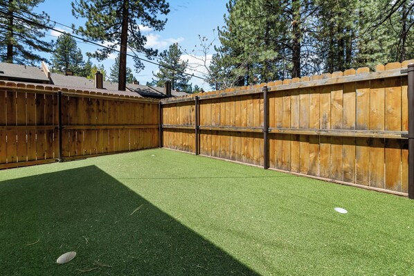 Un patio trasero cercado con césped artificial y una valla de madera.