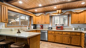 A kitchen with wooden cabinets, a stainless steel dishwasher, and a bar area with stools. - Summit Mountain Lodge (Big Bear Lake)