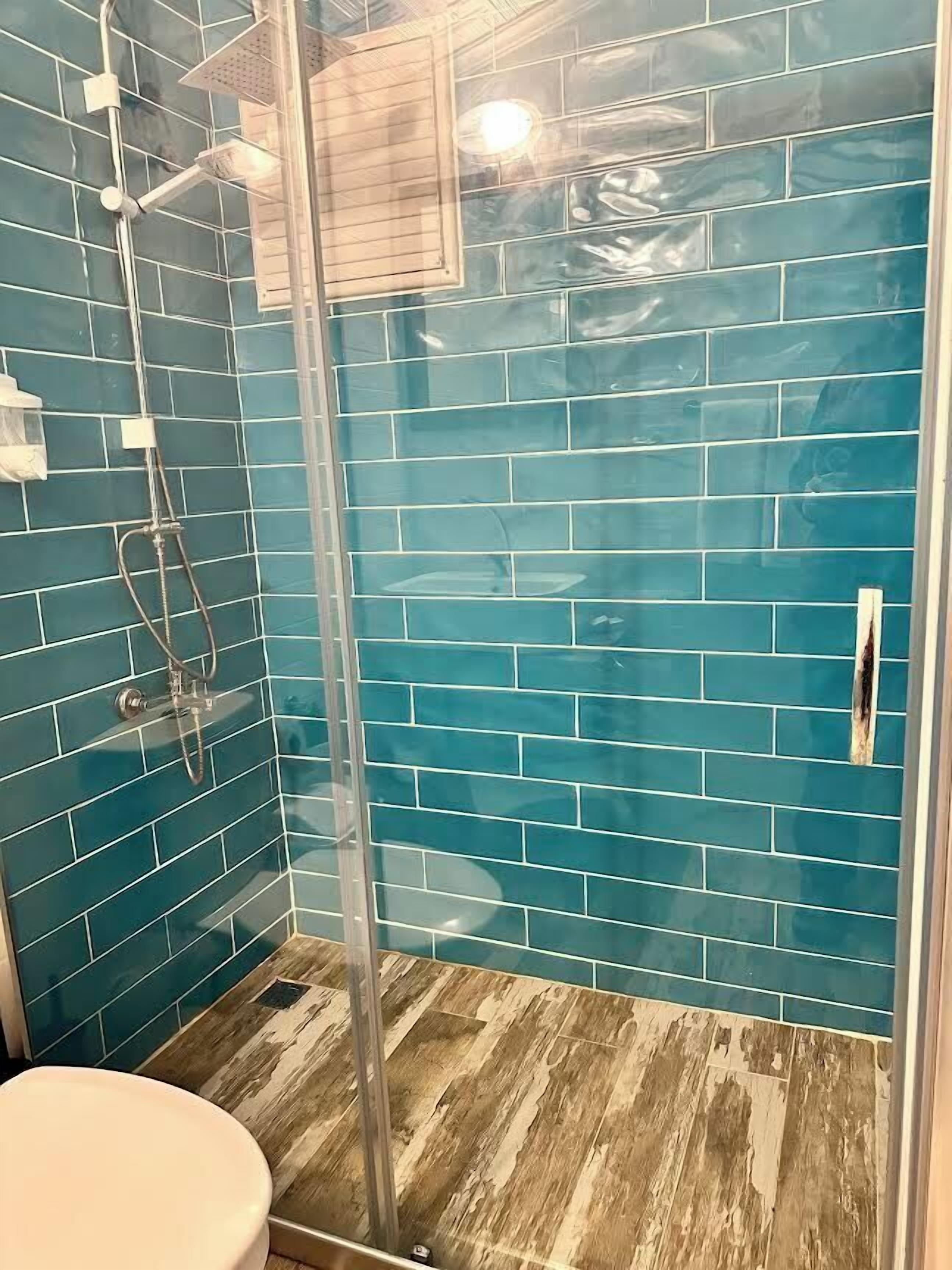 Une salle de bain avec des murs recouverts de carreaux bleus, une douche en verre et un plancher en bois.