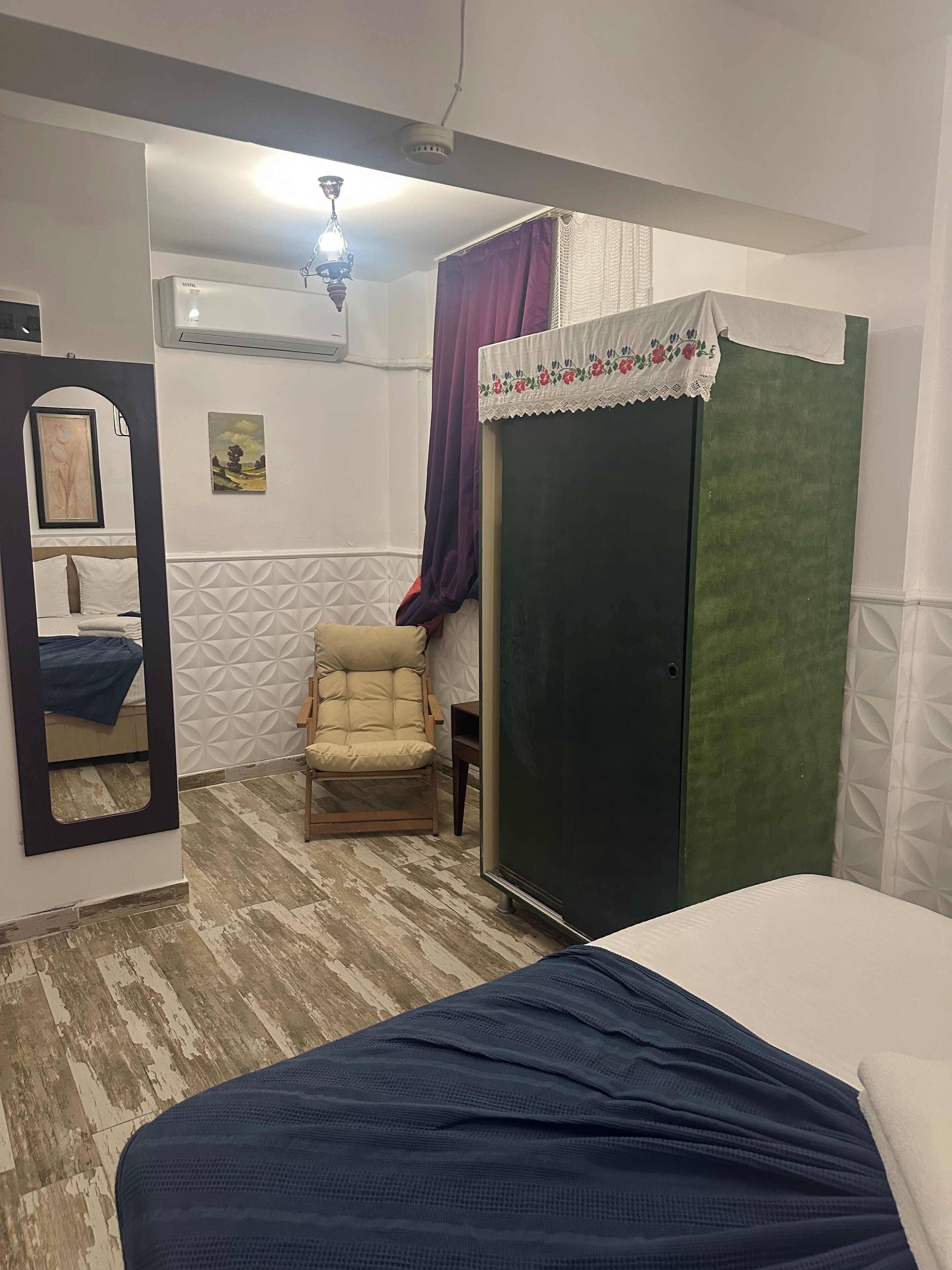 A room with a bed, a chair, a wardrobe, a mirror, and a ceiling fan.