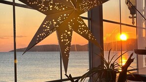 A star-shaped light fixture hanging by a window overlooking a body of water at sunset. - Apelles Butik Otel (Seferihisar)