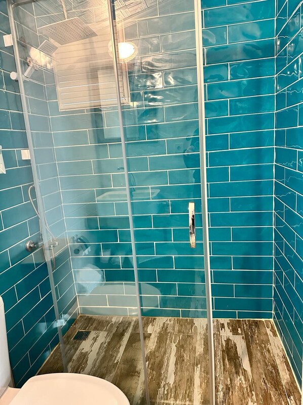 Una ducha con paredes de azulejos azules y suelo de madera, envuelta en vidrio.