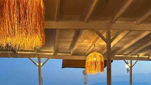A seaside restaurant with wooden tables and chairs, a laptop on one table, and a view of the ocean. - Apelles Butik Otel (Seferihisar)