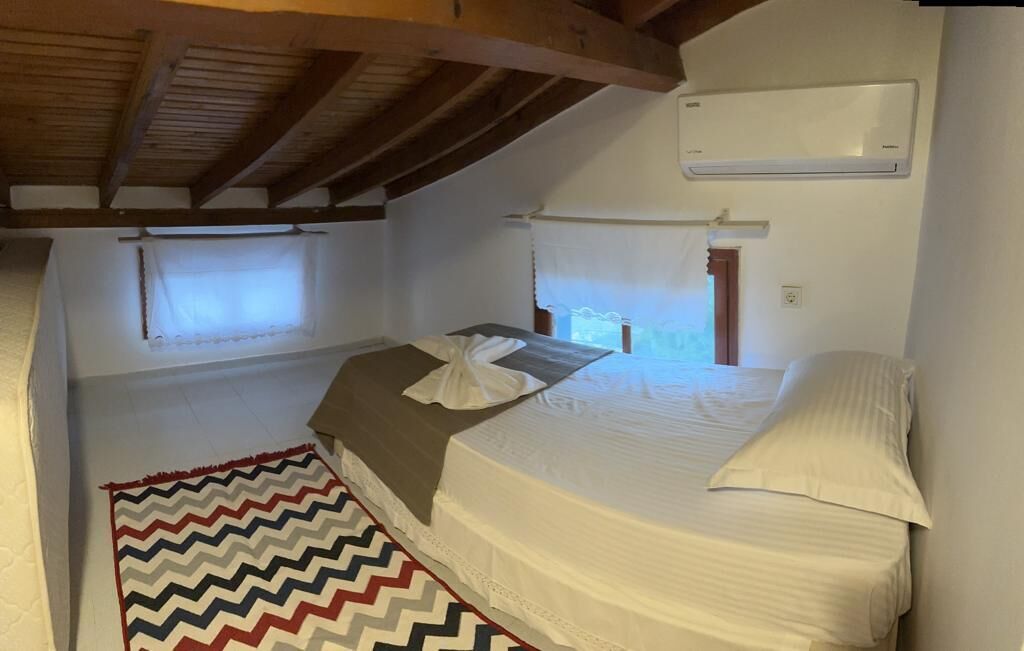 Un dormitorio con cama, ventana, equipo de aire acondicionado y una alfombra de estampado en zigzag.