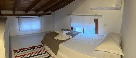 Un dormitorio con cama, ventana, equipo de aire acondicionado y una alfombra de estampado en zigzag.