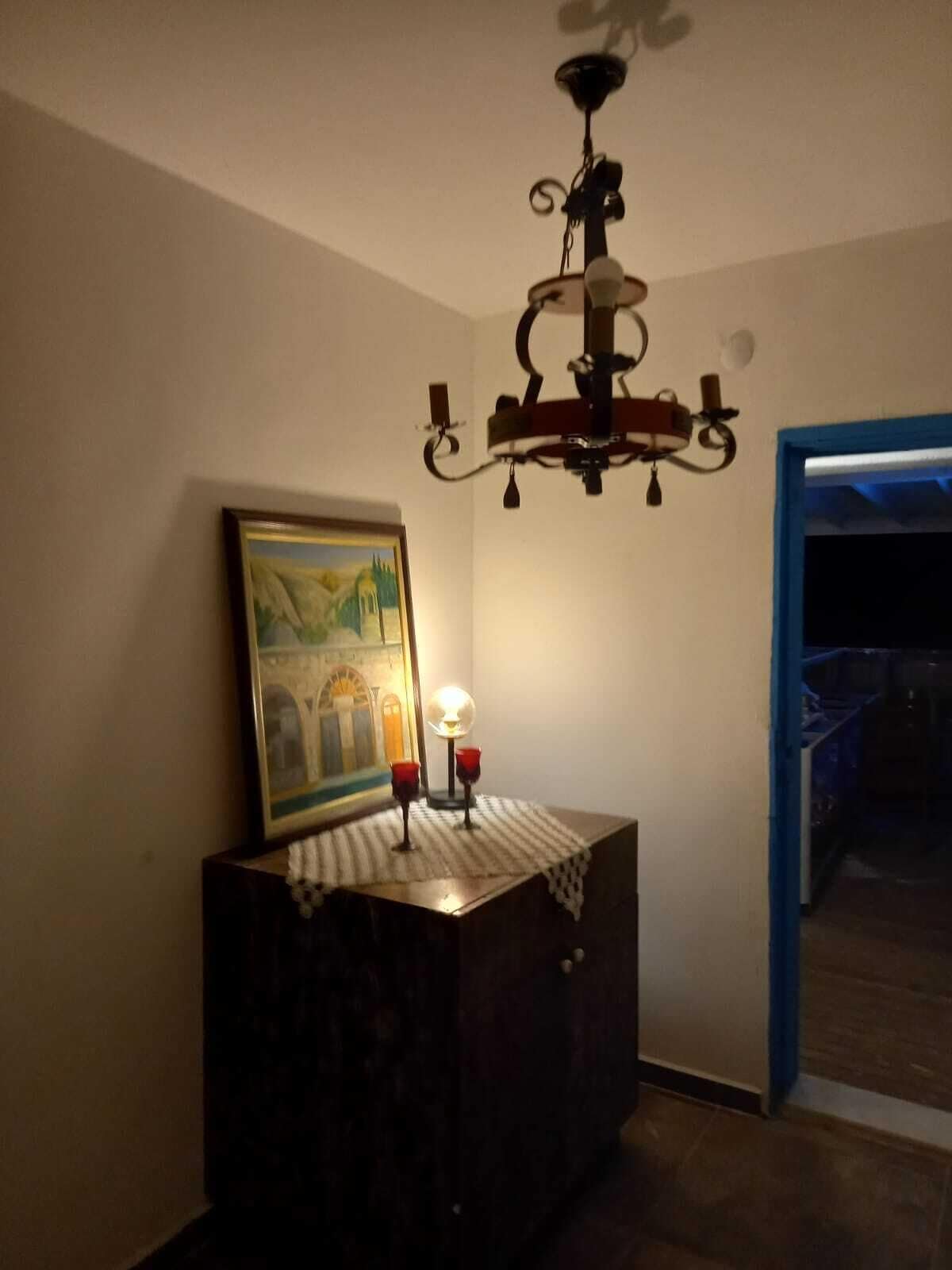 Una habitación con una araña, un cuadro enmarcado y una pequeña mesa con dos velas.