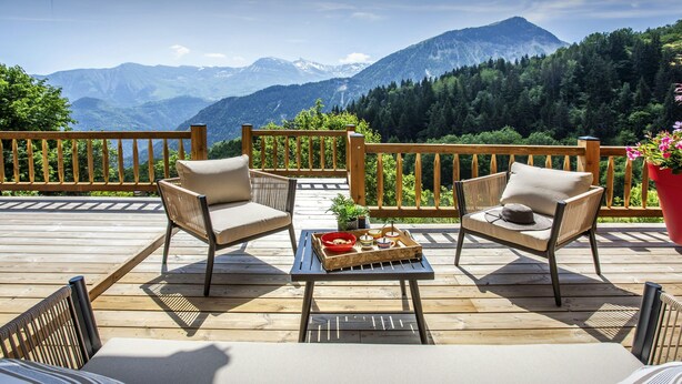 Eine Terrasse mit zwei gepolsterten Stühlen und einem Tisch mit Blick auf eine gebirgige Landschaft.
