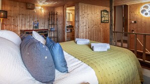 Ein holzgetäfeltes Zimmer im Blockhausstil mit einem Bett, Kissen, einem Nachttisch, einer Lampe und einer Wanduhr.