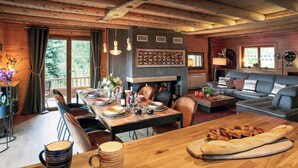 Ein gemütliches Blockhaus-Interieur mit Essbereich, Kamin, Sofa und großem Fenster.