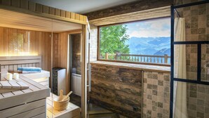 Ein Saunaraum mit Holzbänken, einem Holzeimer und Blick auf Berge durch ein Fenster.