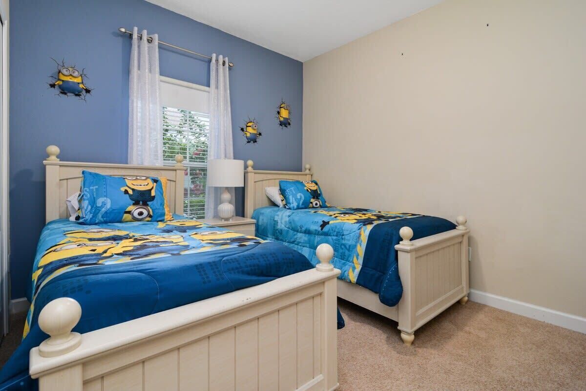 A bedroom with two beds, each with matching blue bedding and Minion-themed decor.