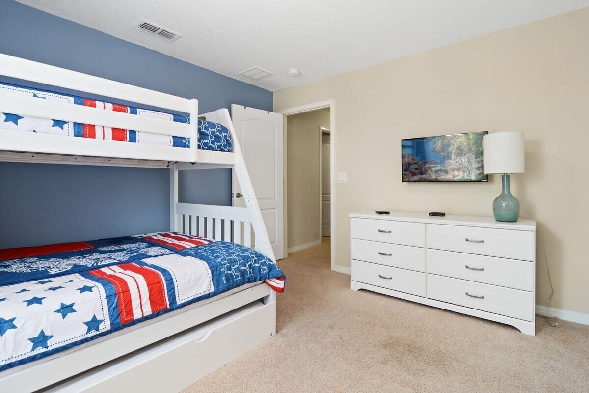 A bunk bed with a patriotic-themed bedding, a white dresser, and a painting on the wall.