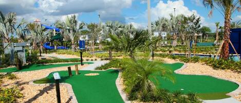 A golf course with a water slide, palm trees, and a clear sky.