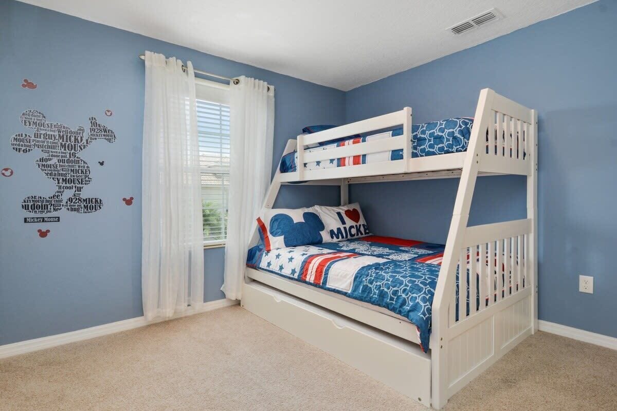 Une chambre pour enfant avec un lit superposé décoré aux couleurs de Mickey Mouse, avec des motifs et des autocollants muraux sur le même thème.