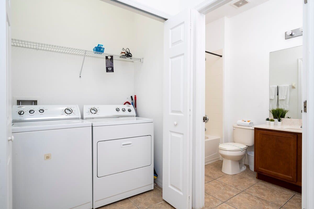 Een wasruimte met een wasmachine en droger, een badkamer met toilet en wastafel, en een douchehoek.