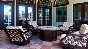 A covered patio area with a round table and four cushioned chairs, large arched windows, and a ceiling fan. - Amazing 4Bd Screened Pool Close to Disney 4572 (Kissimmee)
